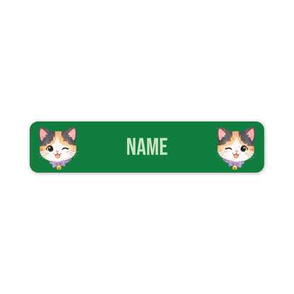 A green rectangular name tag with rounded corners, featuring two cartoon calico cat faces on the left and right sides and the word 'NAME' in the center for personalisation.