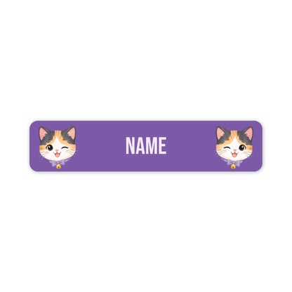 A purple rectangular name label with rounded corners, featuring two cartoon calico cat faces at the left and right edges and the word 'NAME' in white centered on the label.