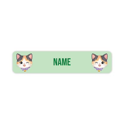 A personalised rectangular label with rounded corners, featuring a light mint green background, the word 'NAME' in green text in the centre, and two cartoon calico cat faces on the left and right sides.