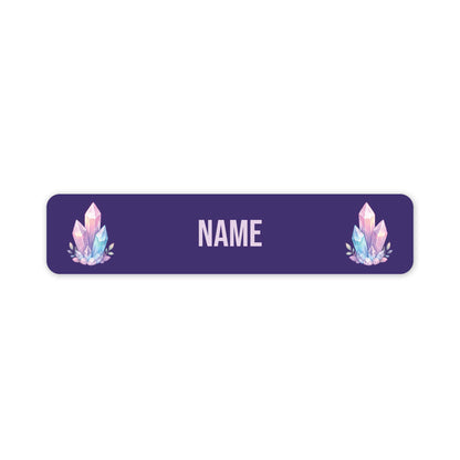 A horizontal rectangular name label with rounded corners, featuring a dark purple background, customisable 'NAME' in the centre, and two matching pastel crystal illustrations on the left and right sides.