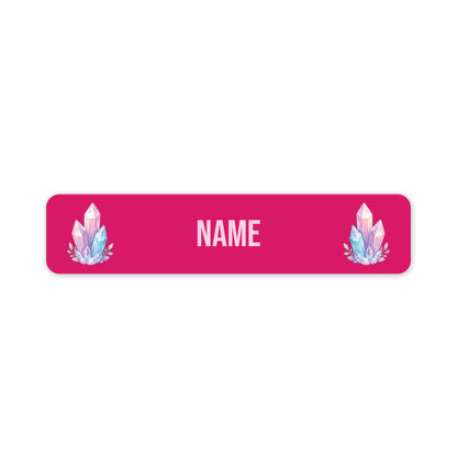 A horizontal rectangular name label with rounded corners, featuring a pink background, customisable 'NAME' in the centre, and two matching pastel crystal illustrations on the left and right sides.