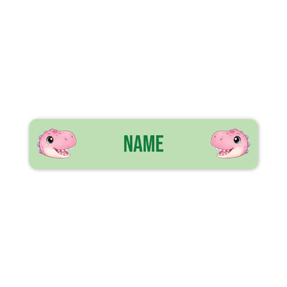 A horizontal light green personalized name label with rounded corners, featuring two pink cartoon dinosaur faces on the left and right sides and the word 'NAME' in green in the center.