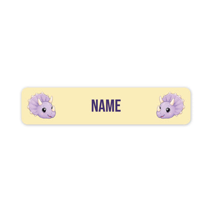 A horizontal pale yellow name label with rounded corners, featuring two cartoon purple triceratops faces at the left and right edges and the word 'NAME' in dark purple text in the center, shown on a white background.