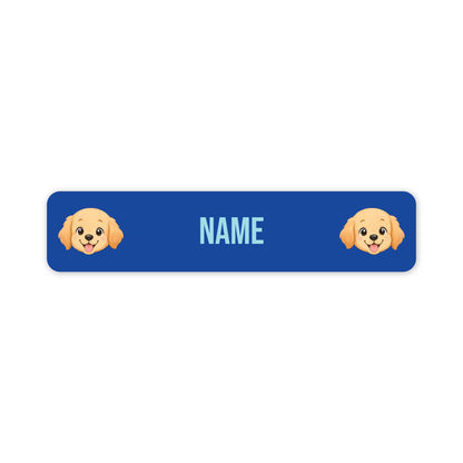 A blue rectangular custom name tag with rounded corners, featuring two cartoon golden retriever dog faces on the sides and the word 'NAME' in light blue in the centre, shown on a plain white background.