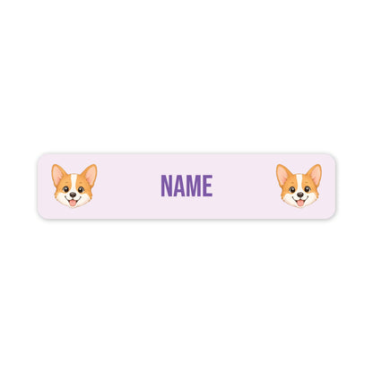 A personalized rectangular label with rounded corners, featuring two cartoon corgi faces on the left and right sides and the word 'NAME' in purple in the center, shown on a plain white background.