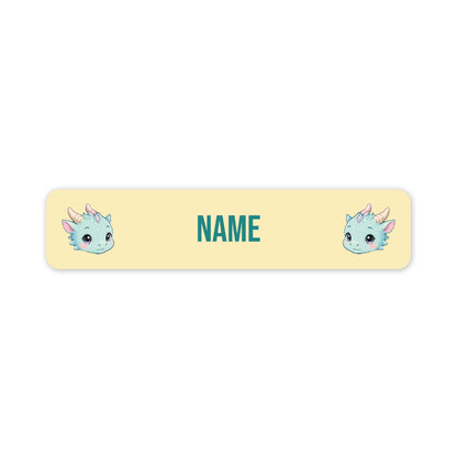 A horizontal name tag with rounded corners, each featuring a cute cartoon dragon illustration on the left and right sides and the word 'NAME' in the centre. The tag is pastel yellow