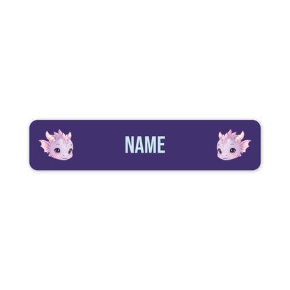 A horizontal purple personalised name label with rounded corners, featuring two cute pink and lavender dragon illustrations on the sides and the word 'NAME' in the centre for customisation.