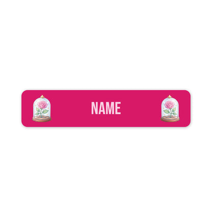 A pink rectangular personalised name plaque with rounded corners, featuring the word 'NAME' in light pink letters in the centre and an illustration of a pink rose under a glass cloche on each side.