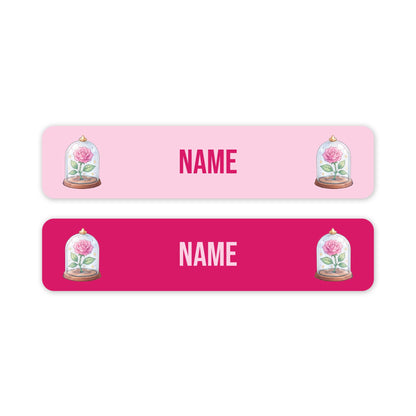 Two horizontal rectangular name labels on a white background. The top label is light pink with the word 'NAME' in pink and pink lettering, flanked by illustrations of pink roses under glass domes.