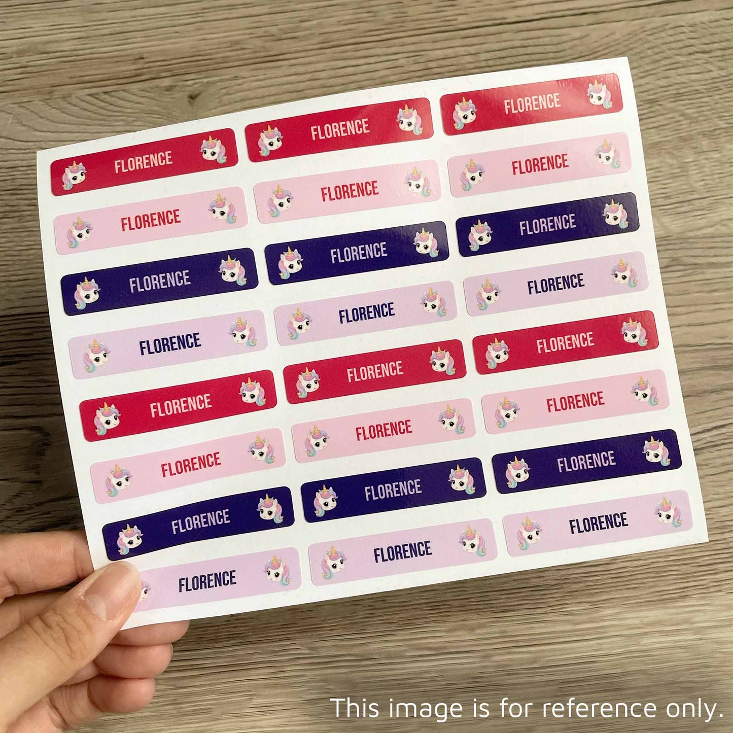 A hand holds a sheet of rectangular stickers with the name 'FLORENCE' repeated in red, pink, and purple rows, each accompanied by a small cartoon fox face. The sheet is photographed on a wood surface.