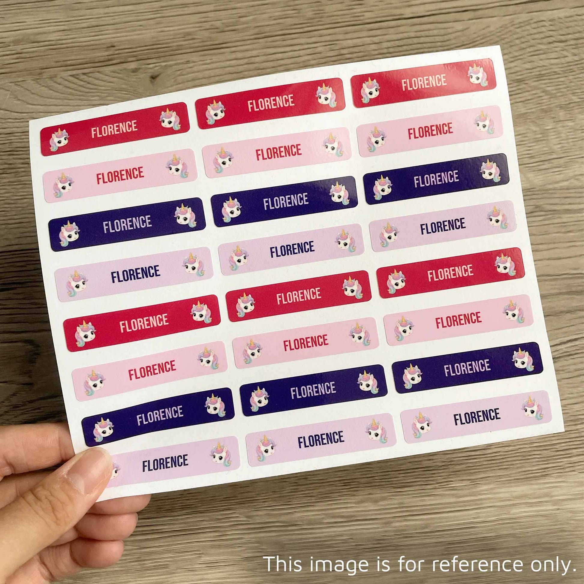 A hand holds a sheet of rectangular stickers with the name 'FLORENCE' repeated in red, pink, and purple rows, each accompanied by a small cartoon fox face. The sheet is photographed on a wood surface.