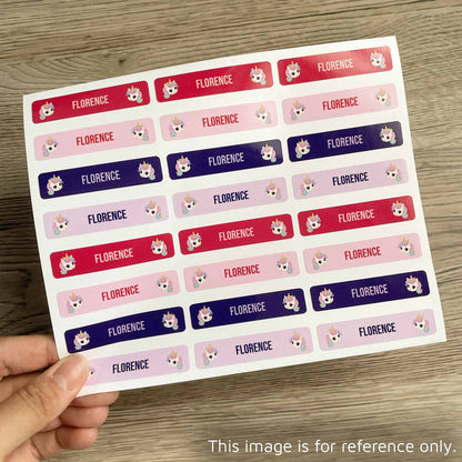 A hand holds a sheet of rectangular stickers with the name 'FLORENCE' repeated in red, pink, and purple rows, each accompanied by a small cartoon fox face. The sheet is photographed on a wood surface.
