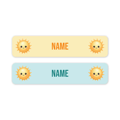 Two horizontal name tags with rounded corners on a white background. The top tag is pale yellow and bottom is pale blue, both have orange cartoon sun icons on both side. Both labels have customisable 'NAME' in the centre.