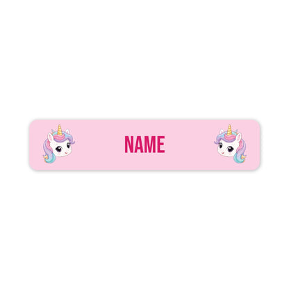 A pink rectangular name label with rounded corners, featuring two cartoon unicorn faces and the word 'NAME' in the center, shown on a plain white background.