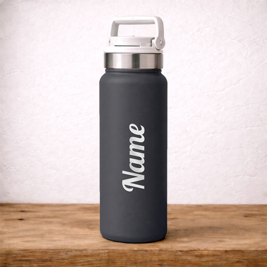 Black water bottle with silver custom 'Name' decal placed on it, placed on a wooden surface with a light background